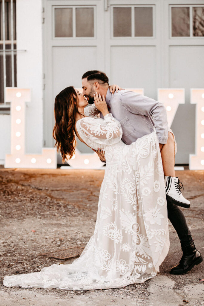 Was ist eine Hochzeitsmesse und lohnt sich ein Besuch? 17 Brautpaar küsst sich vor LOVE Buchstaben